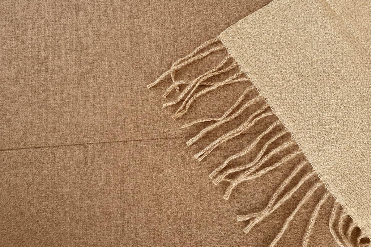 A close-up of a woven scarf in a light oatmealand reverse camel with fringed edges