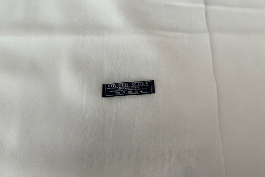 A close-up of white scarf with a small black woven label reading 'VIRGIN WOOL' and additional care text.