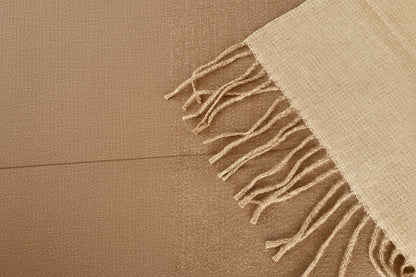A close-up of a woven  scarf in a light oatmealand reverse camel with fringed edges