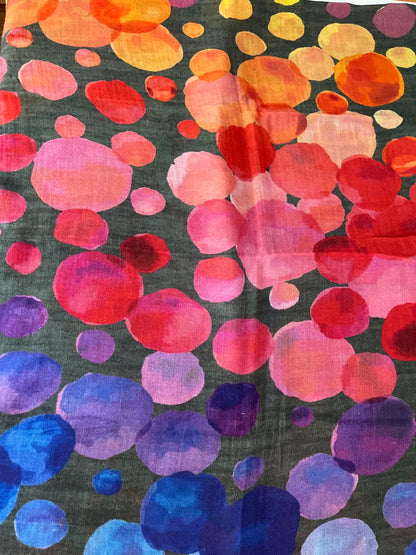 A close-up of a colourful scarf in  abstract watercolor-style pattern of overlapping circles in orange, yellow, red, pink, purple, and blue on a dark charcoal background.