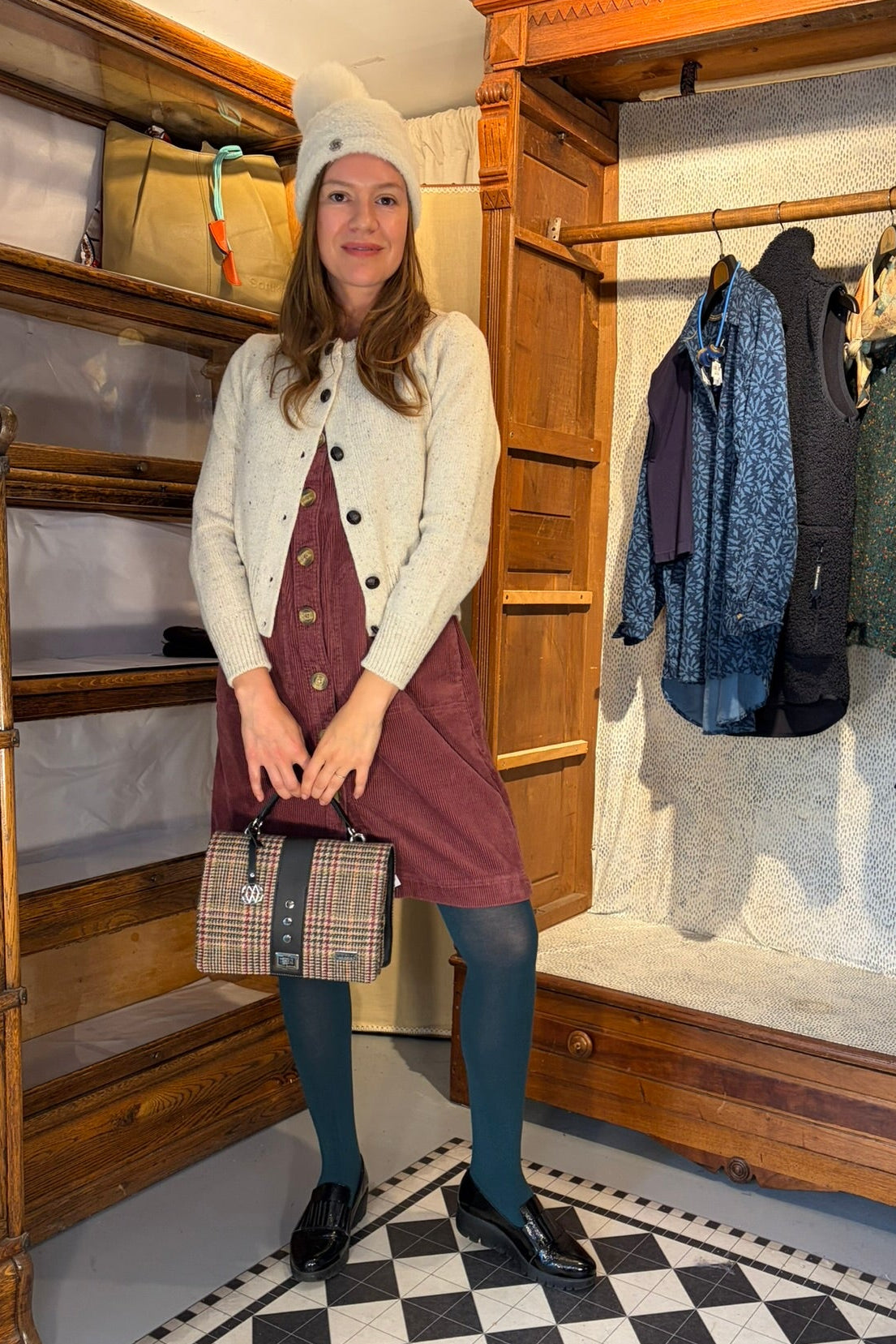 Cari wearing the Junge Sophie Duffel Coat over the Cassia cardigan and White Stuff Millie Cord Shift Dress, with teal tights, an alpaca pompom hat and the Mucros Fiona bag