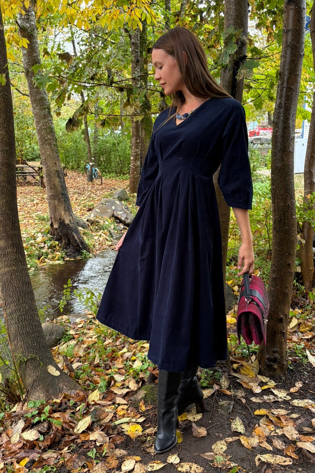 Cari wearing the White Stuff Kate Cord Dress by the stream with the pink plaid Mucros Fiona bag and Spring Moon Starry Night necklace