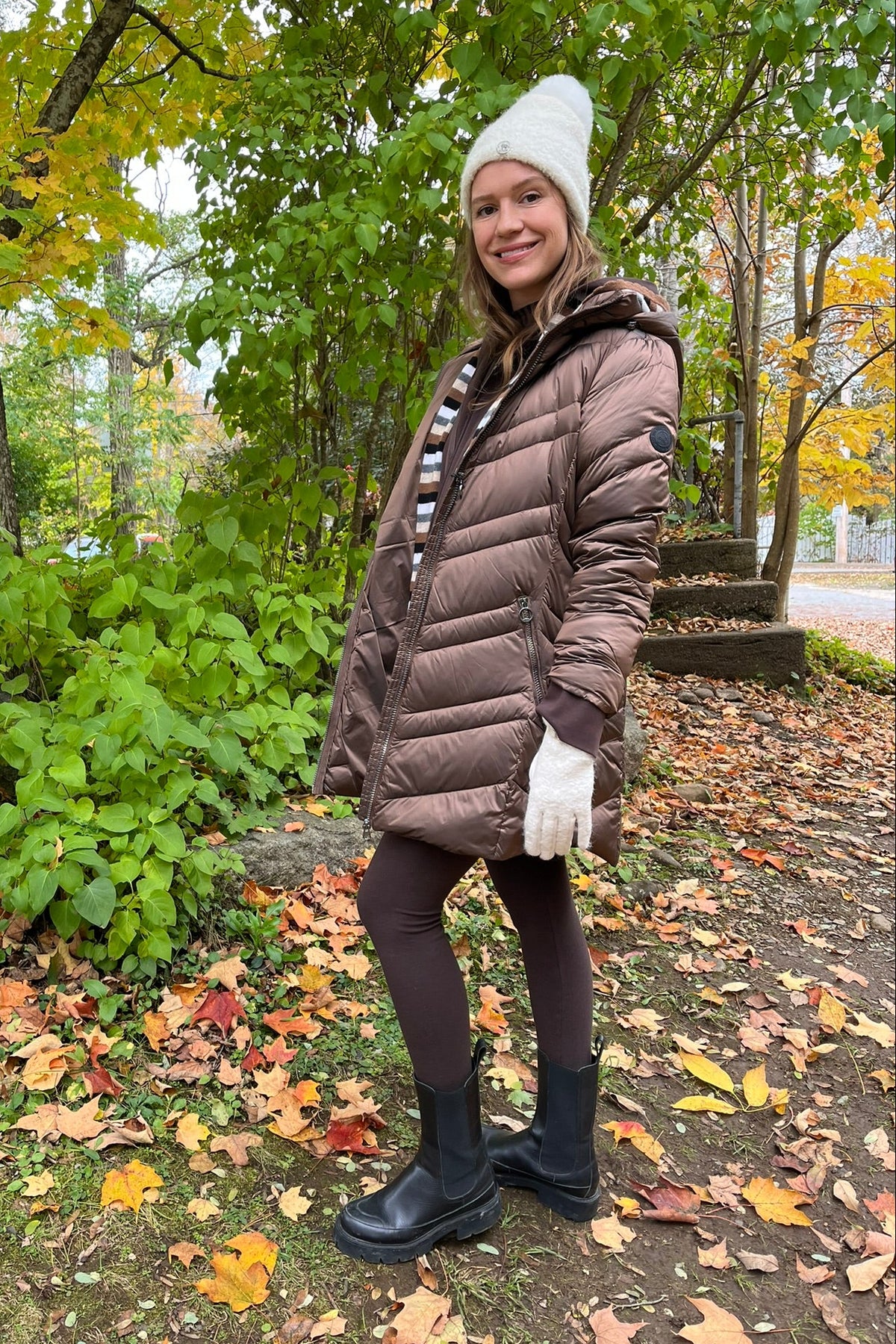 Cari wearing the Junge Phillipa down coat in brown over a Blue Sky Cortes jacket, LUUKAA stripe pullover and HUE leggings, with a Maison Izzy hooded scarf, alpaca pompom hat and LUV & Co. gloves