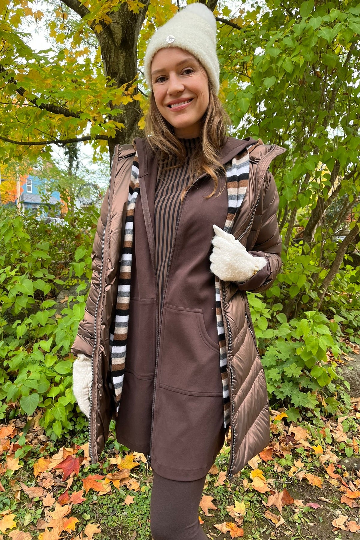Cari wearing the Junge Phillipa down coat in brown over a Blue Sky Cortes jacket, LUUKAA stripe pullover and HUE leggings, with a Maison Izzy hooded scarf, alpaca pompom hat and LUV & Co. gloves