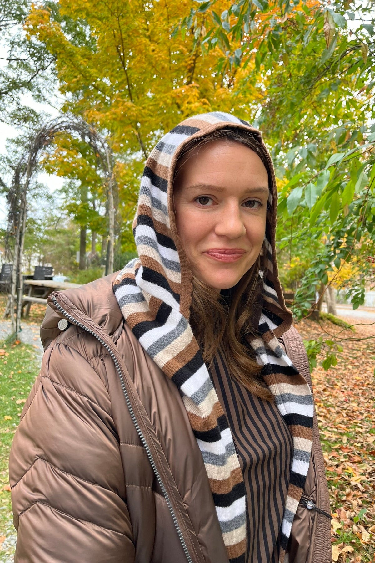 Cari wearing the Junge Phillipa down coat in brown over a Blue Sky Cortes jacket, LUUKAA stripe pullover and HUE leggings, with a Maison Izzy hooded scarf, alpaca pompom hat and LUV & Co. gloves