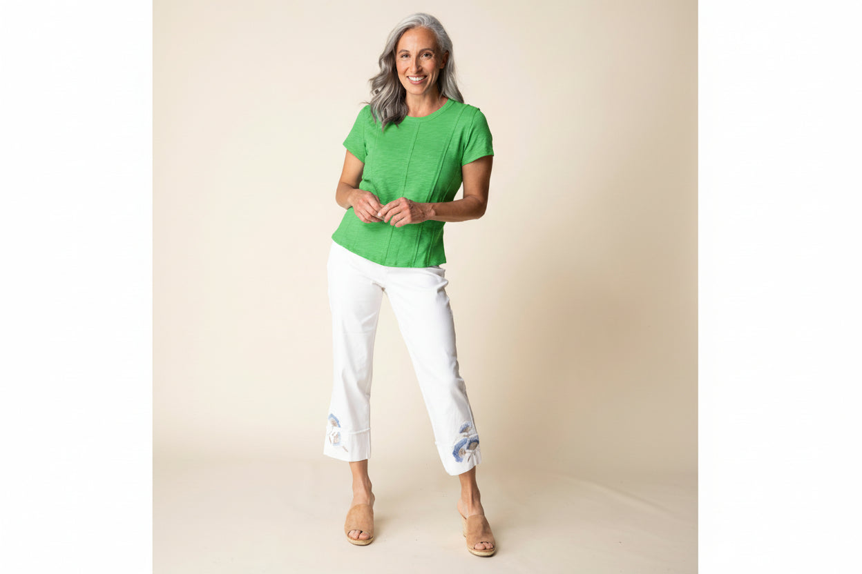 Woman wearing a light blue top and white pants with floral embroidery on a beige background