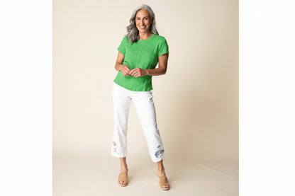 Woman wearing a light blue top and white pants with floral embroidery on a beige background