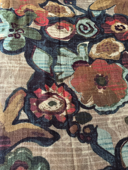 A close-up of a floral patterned scarf with large stylized flowers in red, brown, green, and light blue on a beige woven background.