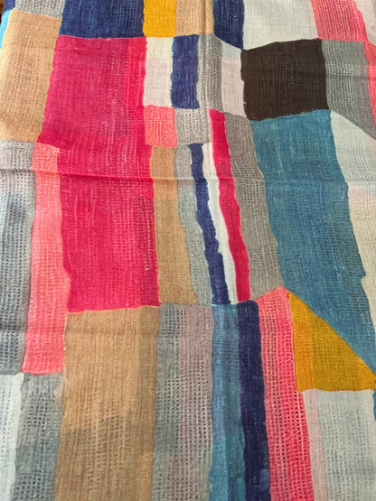 A close-up of a multicolor patchwork scarf with woven rectangular blocks in pink, blue, beige, gray, white, yellow, and brown.