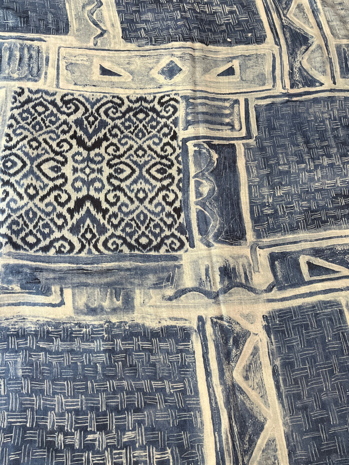 A close-up of a textile scarf  featuring a denim indigo  blue and cream patchwork design with geometric and ikat-inspired patterns.