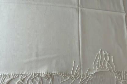 A close-up of a white woven scarf with fringed edge.