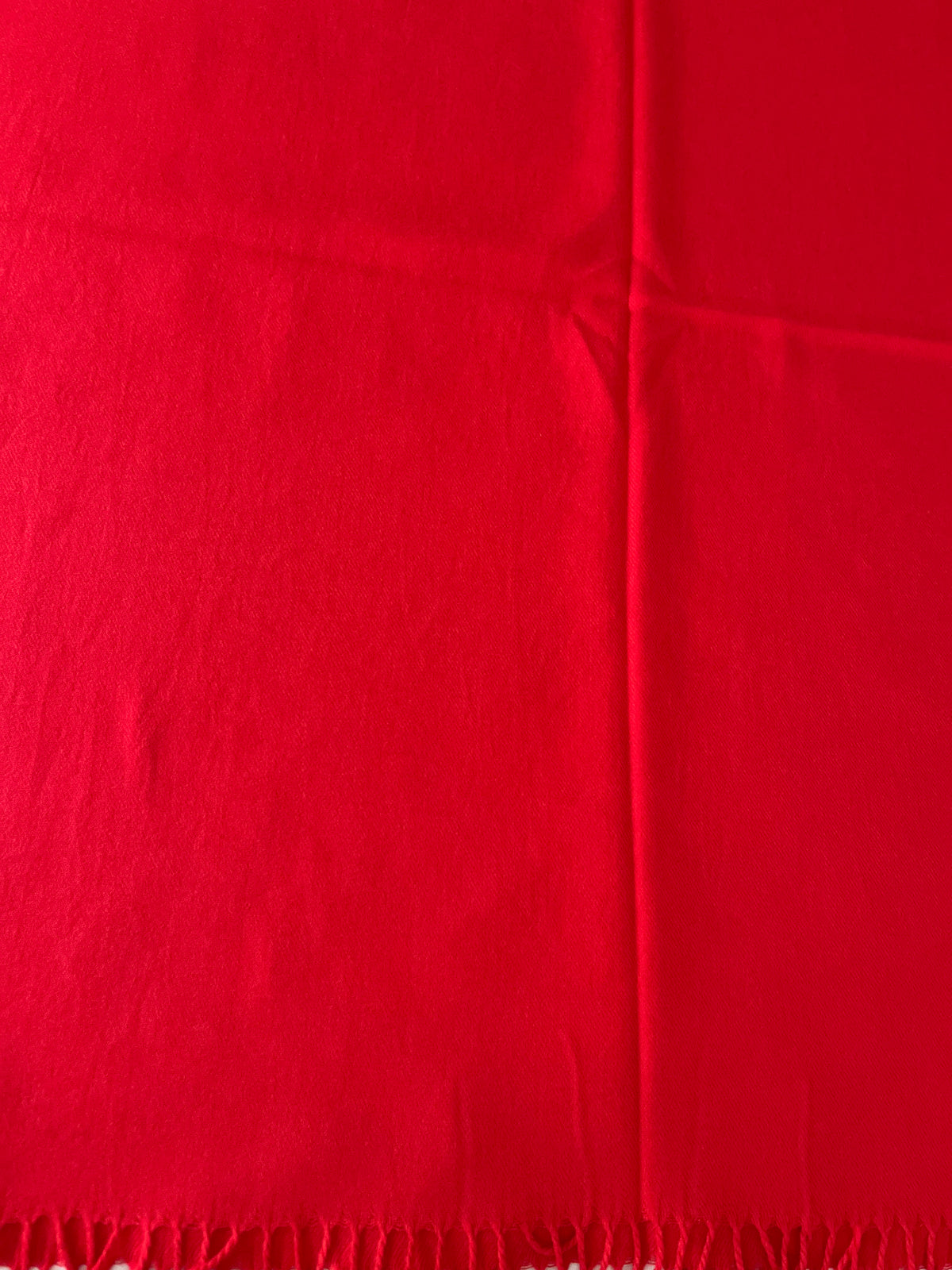 A close-up of a bright red scarf  and fringed edge along the bottom.