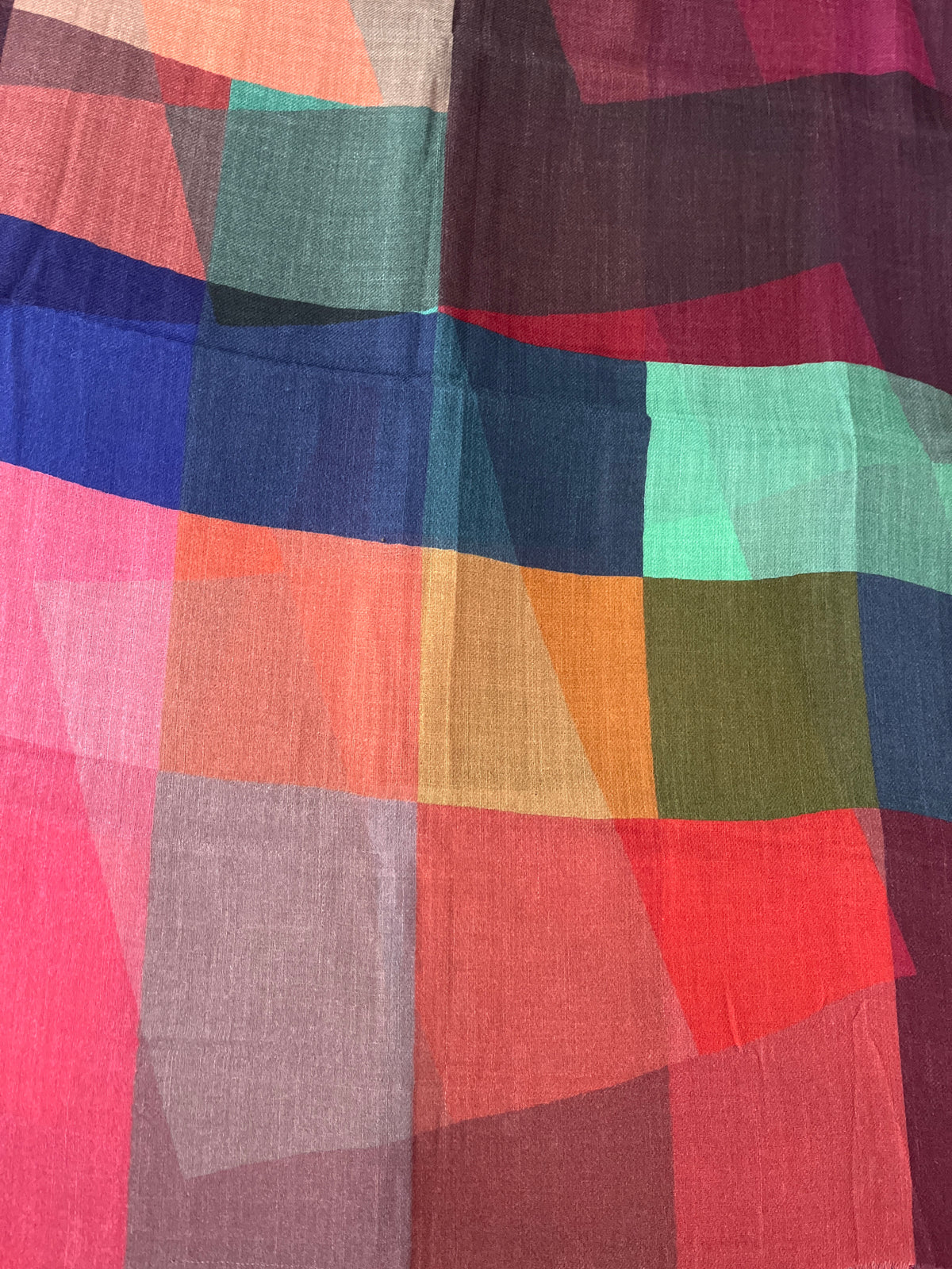 A close-up of a lightweight scarf with an abstract geometric patchwork pattern in multiple colors including pink, red, orange, blue, green, and purple.