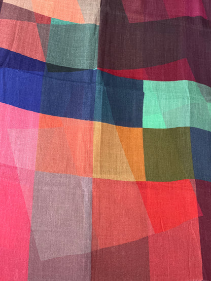 A close-up of a lightweight scarf with an abstract geometric patchwork pattern in multiple colors including pink, red, orange, blue, green, and purple.