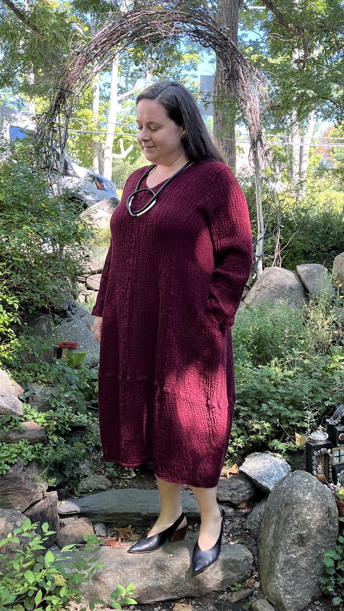 Alma in the Suttles garden wearing the Grizas heavy linen dress in raspberry with a Pursuits Infini cord necklace