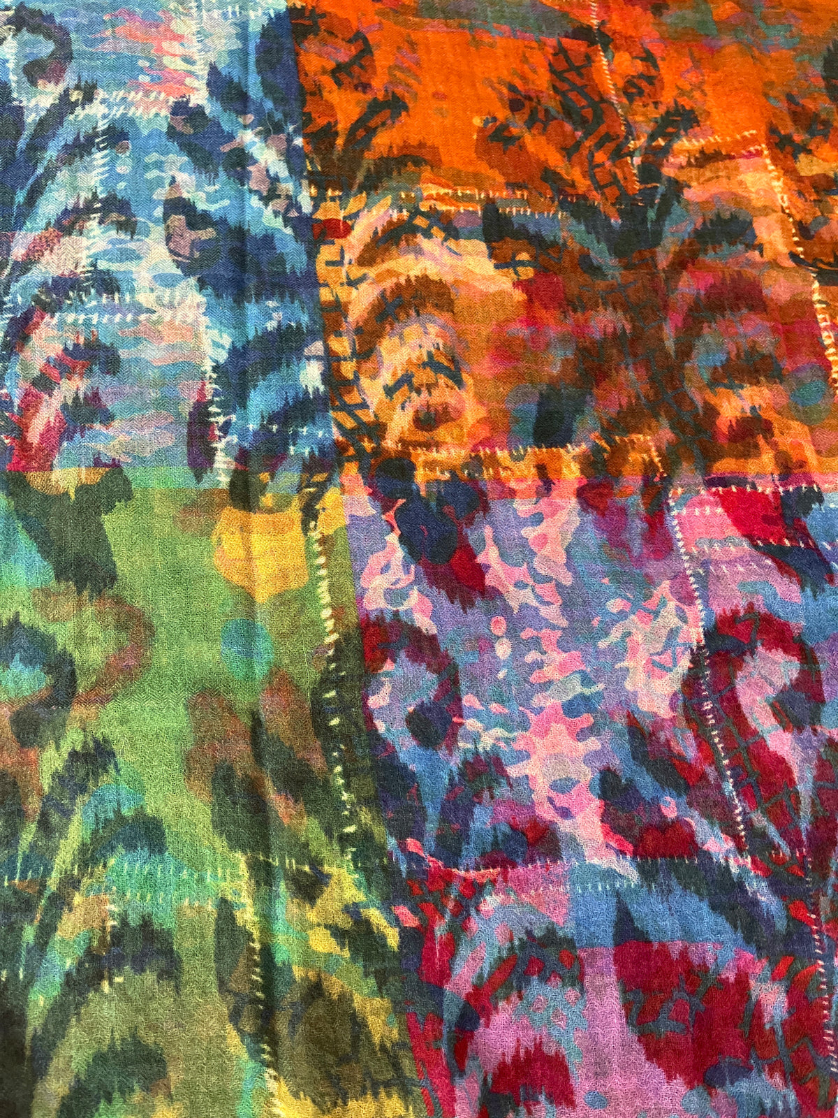 A close-up of a colorful scarf print with an abstract, painterly pattern in blue, green, orange, pink, purple, and red, featuring fern details