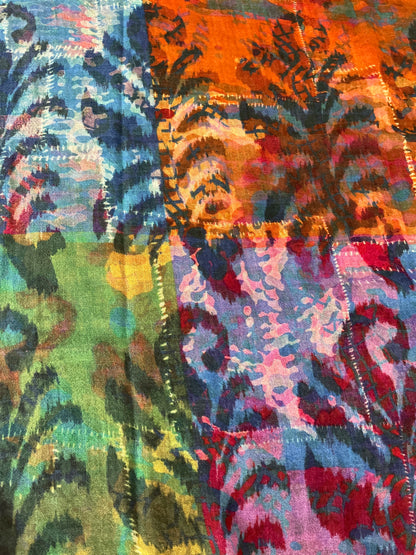 A close-up of a colorful scarf print with an abstract, painterly pattern in blue, green, orange, pink, purple, and red, featuring fern details