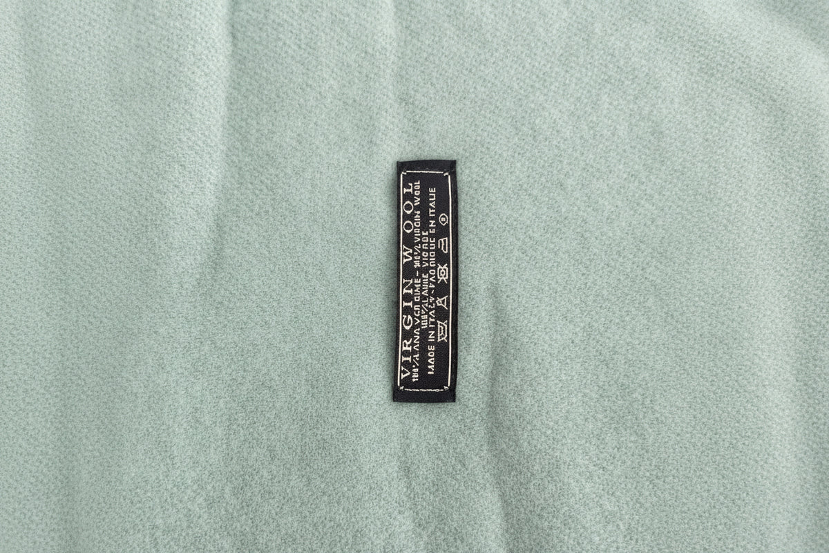 Close-up of aaqua heather knit scarf with a small black woven label reading 'VIRGIN WOOL' and care symbols.