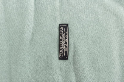 Close-up of aaqua heather knit scarf with a small black woven label reading 'VIRGIN WOOL' and care symbols.