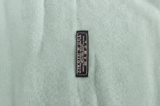 Close-up of aaqua heather knit scarf with a small black woven label reading 'VIRGIN WOOL' and care symbols.