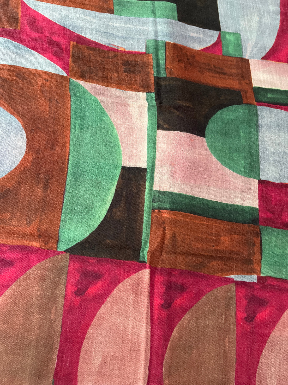 A close-up of a patterned scarf featuring abstract geometric shapes in pink, brown, green, black, white, and beige.