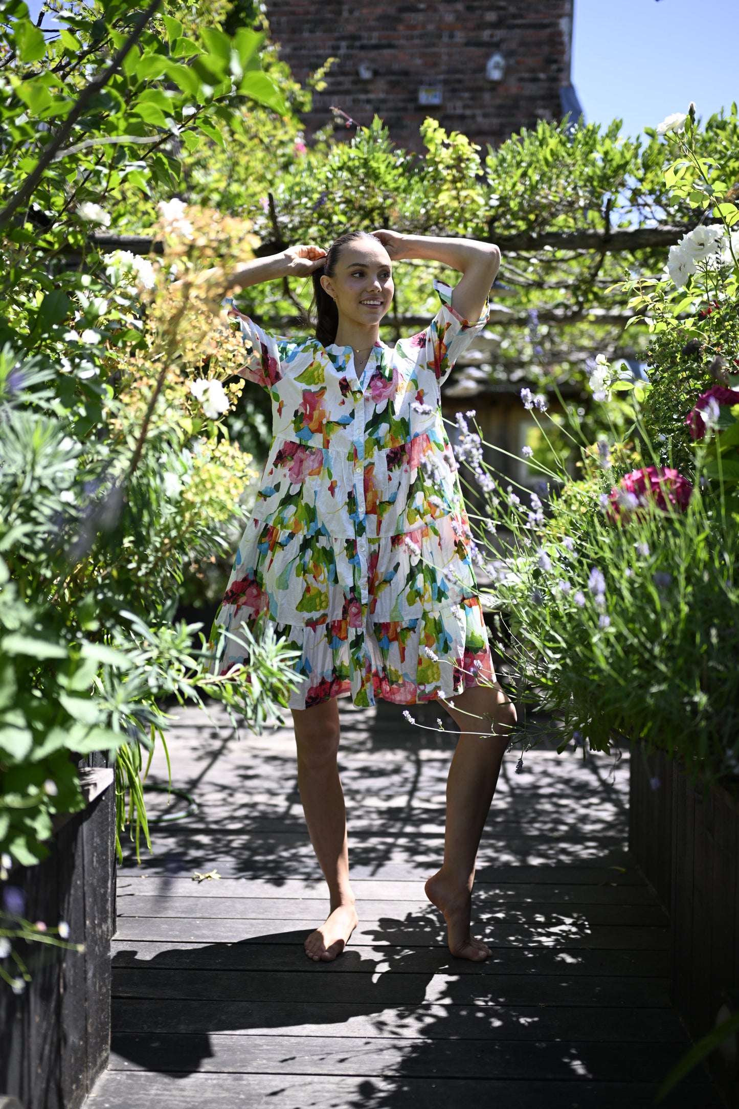 Person wearing a colorful dress standing in a garden with flowers and trees.