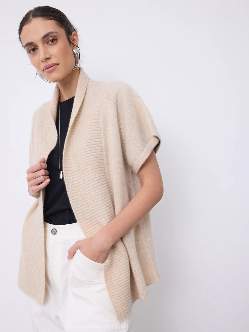Woman wearing a beige cardigan over a black top and white pants on a white background