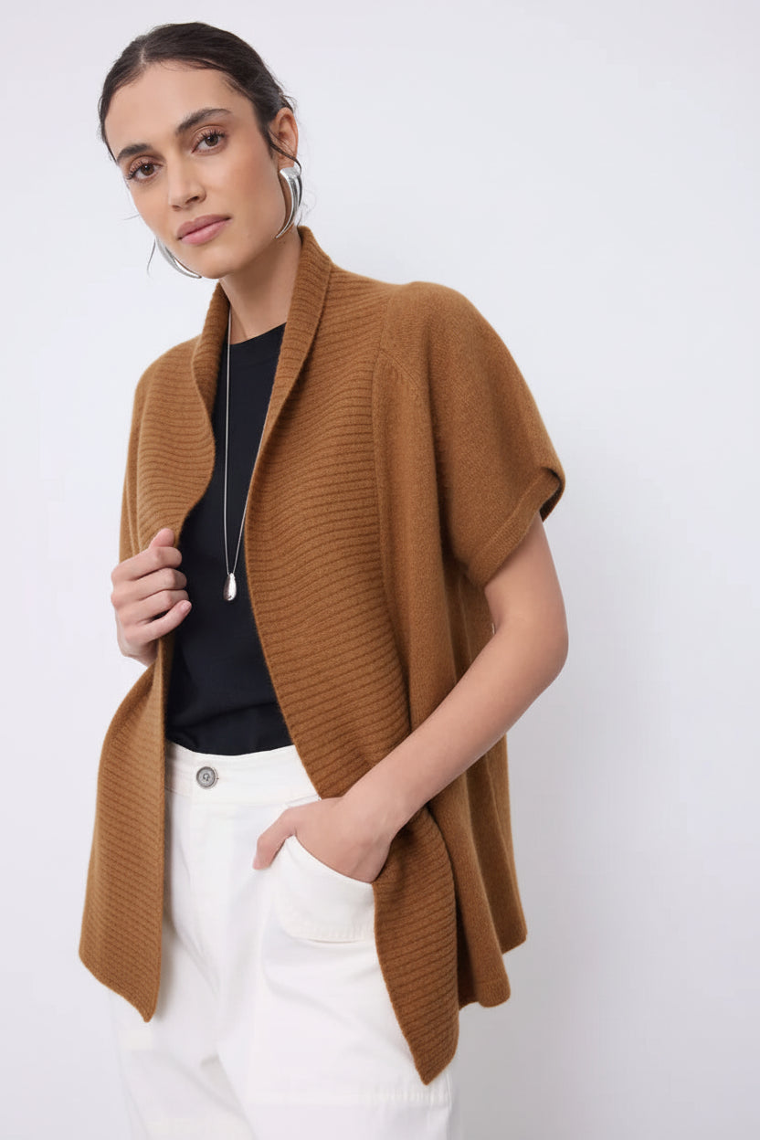 Woman wearing a beige cardigan over a black top and white pants on a white background