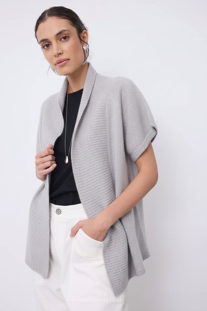 Woman wearing a beige cardigan over a black top and white pants on a white background
