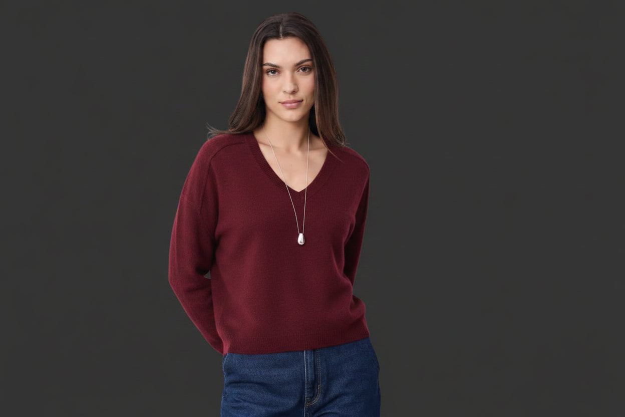 Woman wearing a beige sweater and blue jeans against a white background