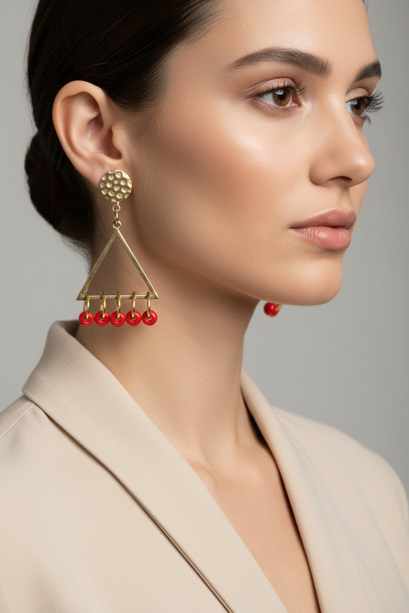 Gold triangle earrings with red beads on a white background