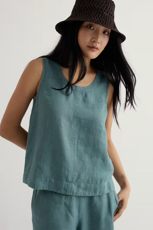 Woman wearing a teal sleeveless top and pants with a brown hat on a white background