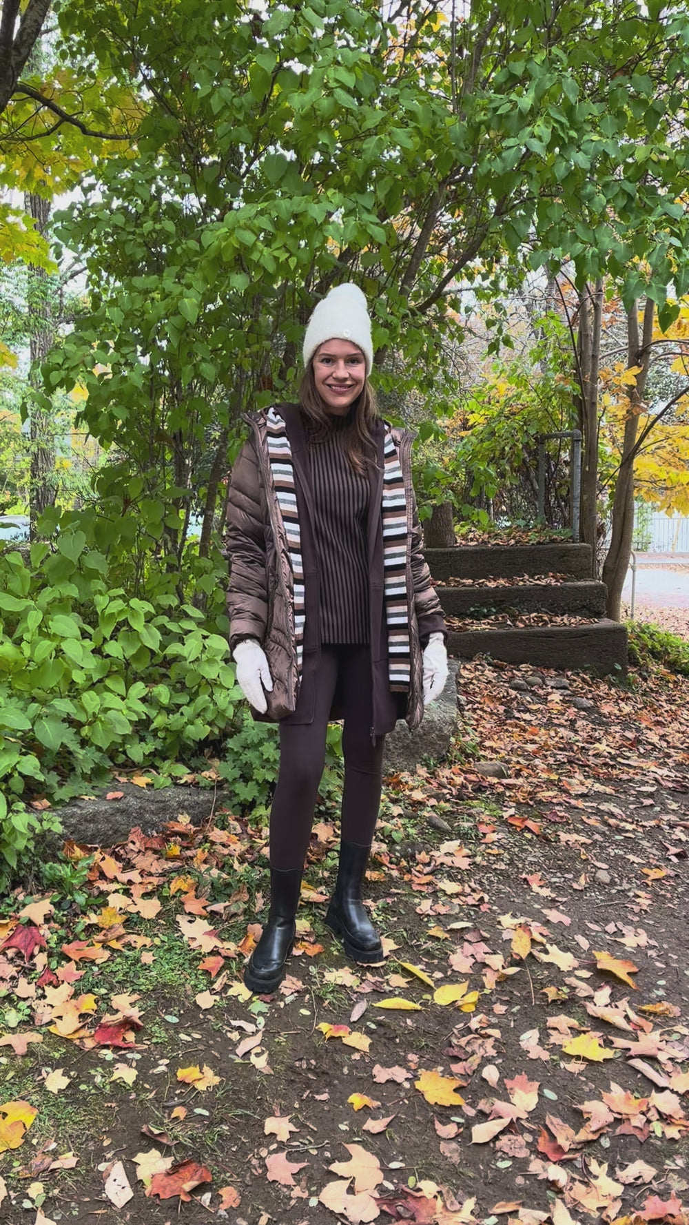 Cari wearing the Junge Phillipa down coat in brown over a Blue Sky Cortes jacket, LUUKAA stripe pullover and HUE leggings, with a Maison Izzy hooded scarf, alpaca pompom hat and LUV & Co. gloves