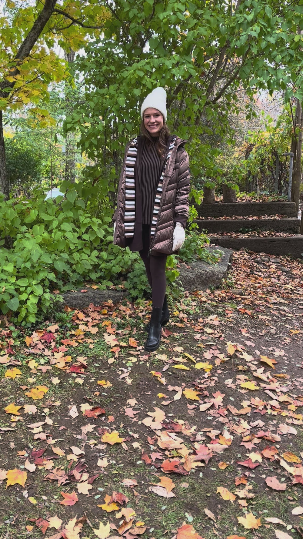 Cari wearing the Junge Phillipa down coat in brown over a Blue Sky Cortes jacket, LUUKAA stripe pullover and HUE leggings, with a Maison Izzy hooded scarf, alpaca pompom hat and LUV & Co. gloves