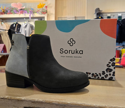 Black ankle boot with gray heel on a wooden surface in front of a Soruka branded box.